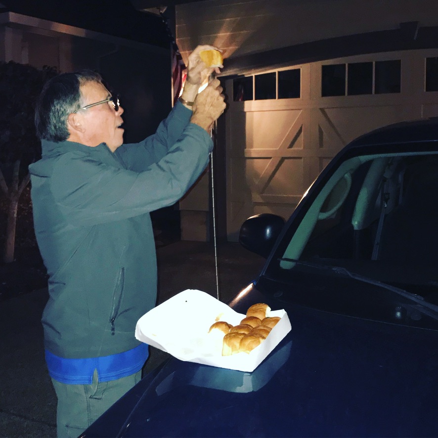 Holding a bun above a car antenna beside a box of fresh rolls.