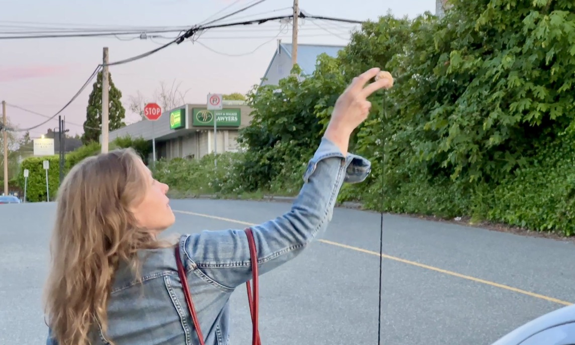 Reaching up to place a bun on a car antenna on a neighborhood street.